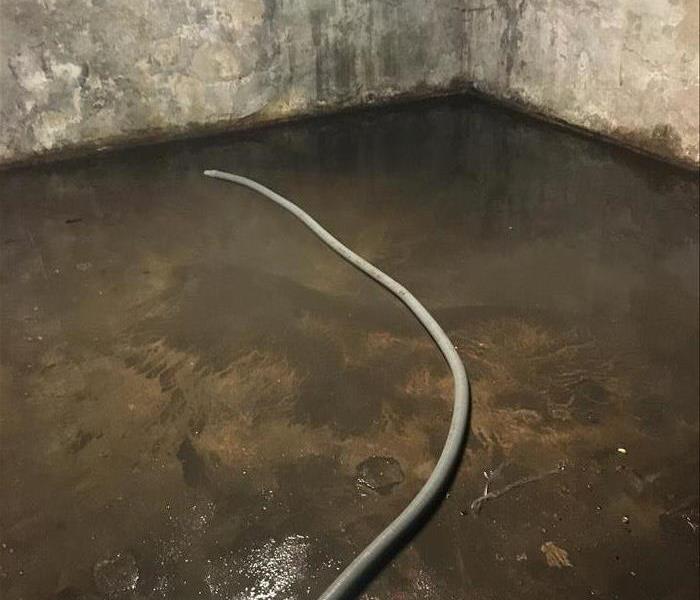 Flooded concrete basement floor from shower drain back up. Hose pump is pumping out the standing water in the basement.