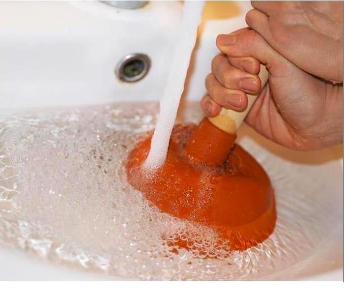 Hand with a plunger unclogging the drain